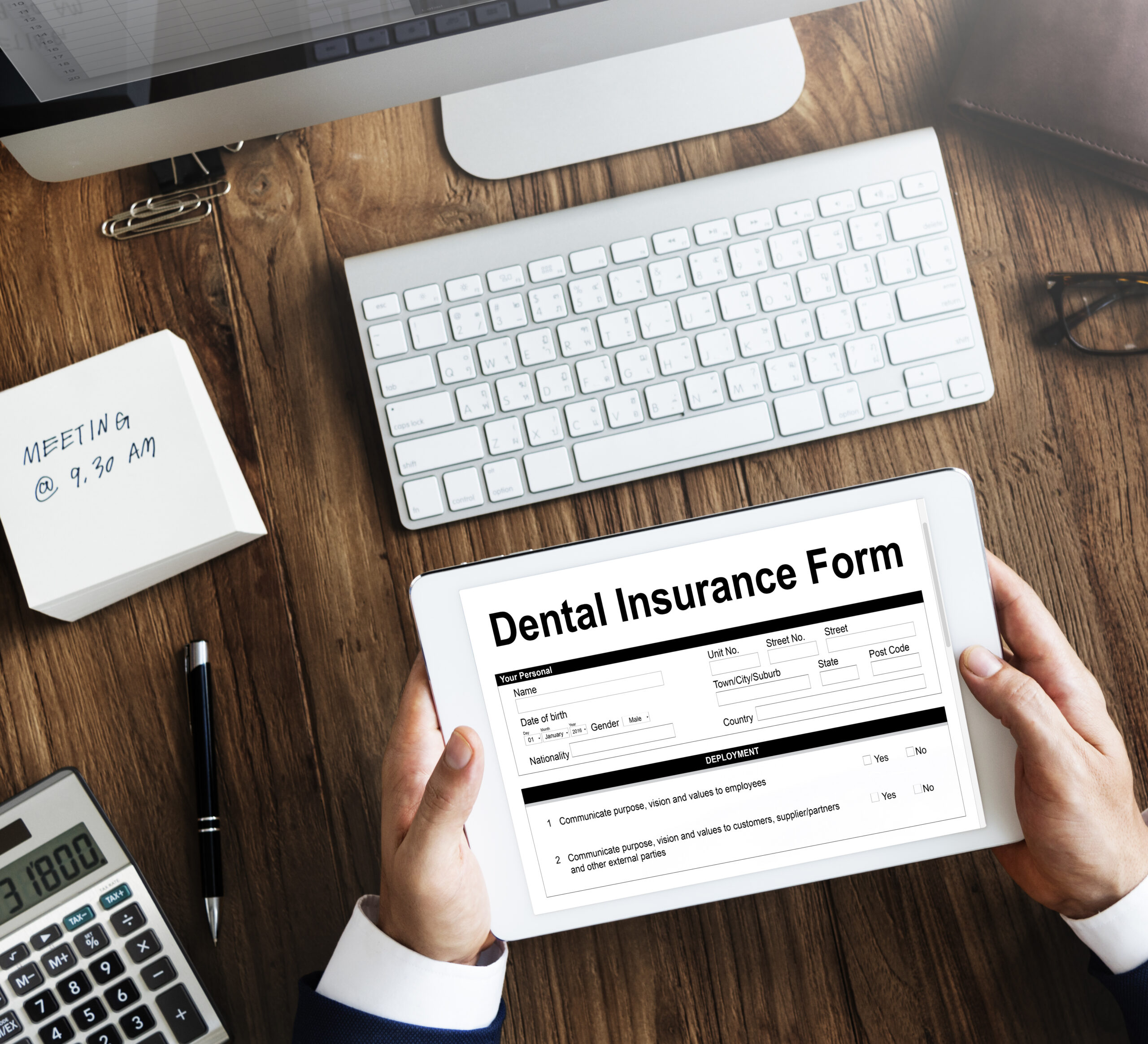 Two hands holding a blank dental insurance form with computer and desk in the background.