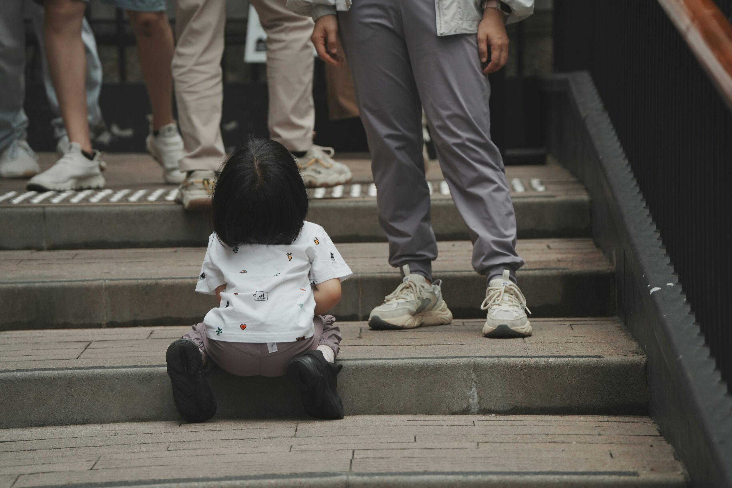 Little girl in crouching position, looking up at adults. You can only see the adults legs in the photo.
